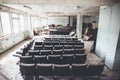 Room with raws of chairs in abandoned and ruined industrial factory, creepy aged building after war, no people