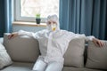 Woman in white workwear and respirator sitting on the sofa
