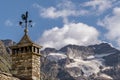 A rooster-shaped weather vane atop a chimney in Lillaz, Aosta Valley, Italy, with the Gran Paradiso glacier in the background