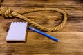 Rope with noose for the suicide, blank notepad and pen on wooden background