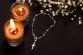 Rosary beads with two blurred orange candles and small flowers, black background, above view Royalty Free Stock Photo