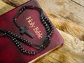A rosary with a Catholic cross and a Holy Bible lie on a wooden table. Prayer, spirituality, faith, catholicism. Holy communion.