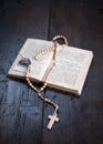 Rosary with cross laying on old open Holy Bible book on rustic wooden table. Christianity, religion, religious symbol. Royalty Free Stock Photo