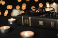 Rosary, glasses on holy bible book and burning candles at night against bokeh light background