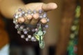 Rosary in one hand. Young junior lady holding rosary with open hand. Female hands holding a rosary with Jesus Christ Cross or Royalty Free Stock Photo