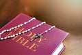 A rosary of white beads with a silver crucifix above the cover of the closed holy bible book. Religion and hope Royalty Free Stock Photo