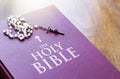 A rosary of white beads with a silver crucifix above the cover of the closed holy bible book. Religion and hope Royalty Free Stock Photo