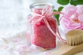 Rose bath salt in glass bottle, body care accessories and fresh rose petals on light background, spa concept