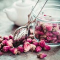 Rose buds tea, tea infuser, glass jar and teapot on background.