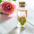 Rose essential oil and rose flowers on white wooden table