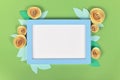 Rose flat lay with blue empty picture frame surrounded by yellow romantic paper craft flowers on green background