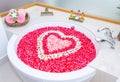 rose petals and leelawadee with heart shape decoration in bathtub and two towel, soap, shampoo, hair cream near bathtub