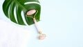 Rose quartz face roller for beauty facial massage therapy with monstera leaf and towel on blue background. Flat lay, top view,