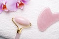 Rose Quartz jade roller and Gua Sha massager on towel on stone background. Close-up. Massage tool for facial skin care, SPA beauty Royalty Free Stock Photo