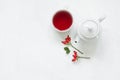 Rosehip glass cup of herbal tea medicinal plants with rosehip branch and ceramic teapot on white table