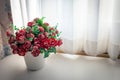 Roses in a vase on a table next to a window lined with white curtains Royalty Free Stock Photo