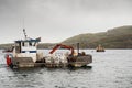 Rosroe Pier, county Galway, Ireland 07/14/2020: Small boat with fish feed on board, Fish industry. Cloudy low sky