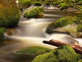 Rot trunk blocked between boulders at stream bank above bright blurred waves. Big mossy stones in clear water of river. Royalty Free Stock Photo