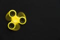 Rotating yellow fidget spinner device on black background.. Top view. Playing with a yellow hand spinner fidget toy