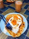 Roti sarang burung, a pratha looks like bird nest with half cook eggs in the middle served with teh tarik as staple breakfast in Royalty Free Stock Photo