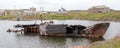 Rotting, abandoned ship on a water of sea bay against the background of an abandoned village, symbols of decadence and degradation