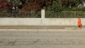 Rough concrete house fence with railing. Plants and flowers on behind, cement sidewalk, red street dustbin and road in front. Royalty Free Stock Photo