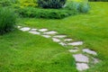 Rough different shapes of natural stone path paved in the green backyard turf lawn. Royalty Free Stock Photo