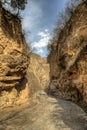 Rough dirt road turns into a paved road in a close canyon with bright blue sky