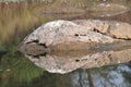 Rough-edged rocks rest at the edge of a calm body of water, casting a clear reflection. Royalty Free Stock Photo
