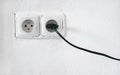 Rough facade white wall with two european style power outlet, one socket plugged black cable Royalty Free Stock Photo