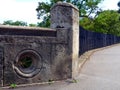 Rough gray stone railing olong public street and black steel fence beyond