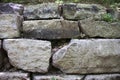 Rough grey stone wall with green grass growing between cracks.