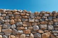 Rough stone wall built with natural rocks stands against clear blue sky. Old masonry structure provides textured surface. Solid Royalty Free Stock Photo