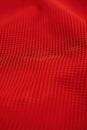Close-up view of red fabric with grid-like pattern. Rough texture and black dots create striking contrast against red background.