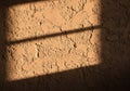 Rough textured beige plaster wall with sunlight casting diagonal shadows. The uneven surface Royalty Free Stock Photo