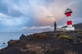 Rough volcanic coastline with old and new lighthouses under the rainbow