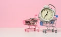 Round alarm clock in a miniature shopping cart with change on a white table. Concept time is money, waste of money and poverty Royalty Free Stock Photo