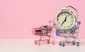 Round alarm clock in a miniature shopping cart with change on a white table. Concept time is money, waste of money and poverty