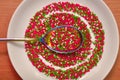 Round baking topping, sprinkle in a white saucer with rainbow spoon on a wooden table, top view