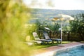 Round beige sunshade and several folding beach chairs by the outdoor pool in agriturismo overlooking fields and farmlands of