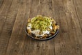 Round black clay bowl with nachos with melted cheese, pico de gallo and guacamole on unglazed wood table