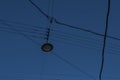 Round black pendant glass lamp hanging from wires over city road against blue sky backdrop. Evening