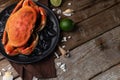 Round black plate with coked king crab in the corner of the photo. Brown napkin. lime. seashells and rustic wooden table