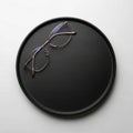 Round black tray with a smooth texture placed on a white surface. A pair of thin metal-framed Royalty Free Stock Photo