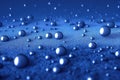 Round blue water drops with reflections falling on a grainy surface.. Royalty Free Stock Photo