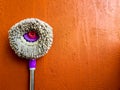 Round broom cloth mop rotary violet handle leaned on orange wall as background with space for text Royalty Free Stock Photo