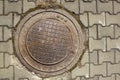 Round brown rusty sewer manhole in gray paving stones with checkered pattern. rough surface texture Royalty Free Stock Photo