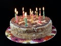 Round cake with candles, on a black background. A sweet birthday present for a teenager. A festive dessert for the whole family