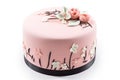 Round cake with pink fondant icing. The cake has a black base and is decorated with white and pink flowers and leaves