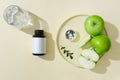 A round ceramic dishes containing green apple and pills on a cap, a medicine bottle and glass cup decorated on a beige background. Royalty Free Stock Photo